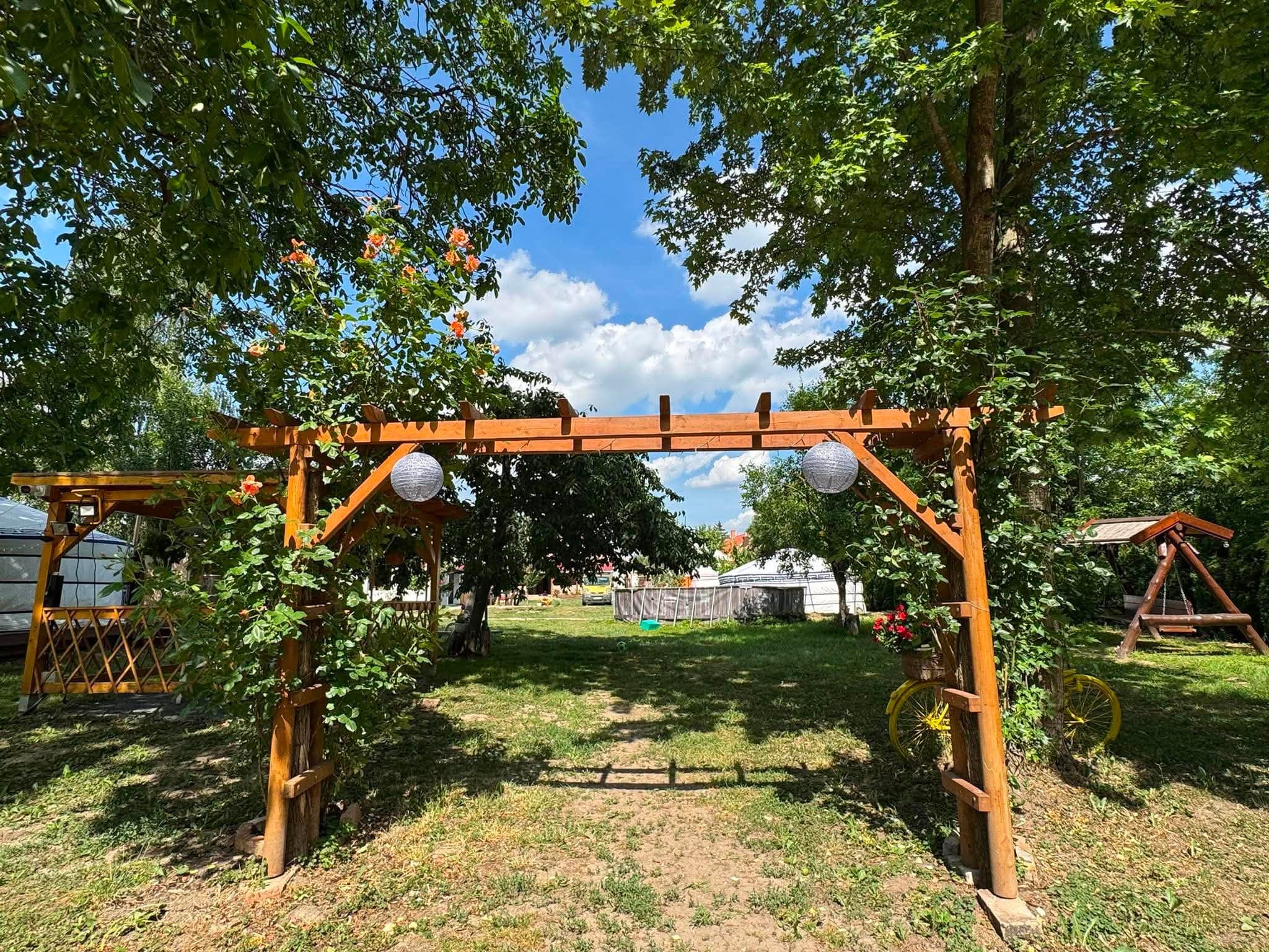 Itgelbirtok – Fa pergola-kapu lámpákkal és futórózsával, mögötte a kert